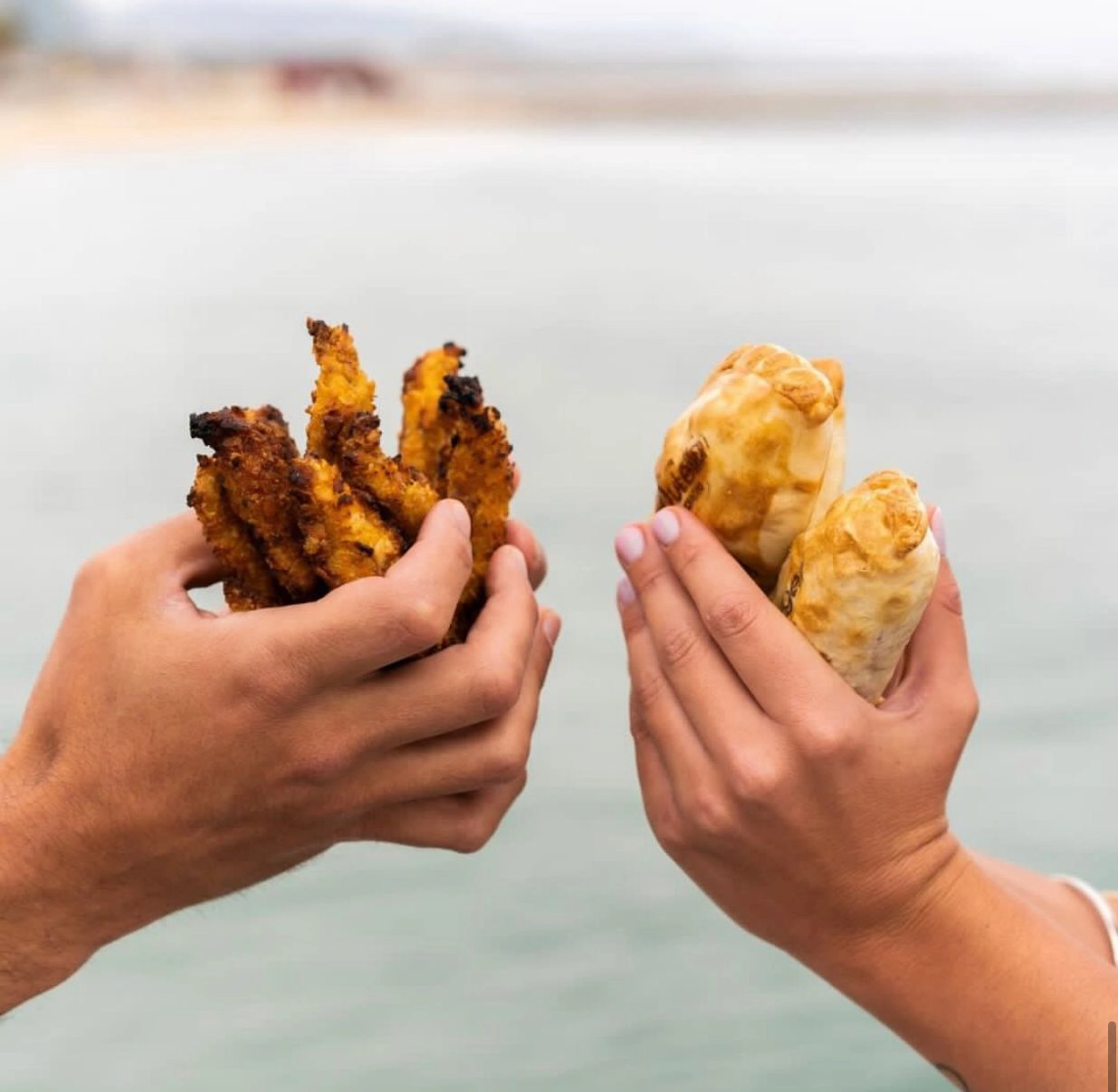 Foto de Fingers de pollo sostenida por unas manos como si fuese un ramo y en las otras manos dos empanadas, ambas manos enfrentadas